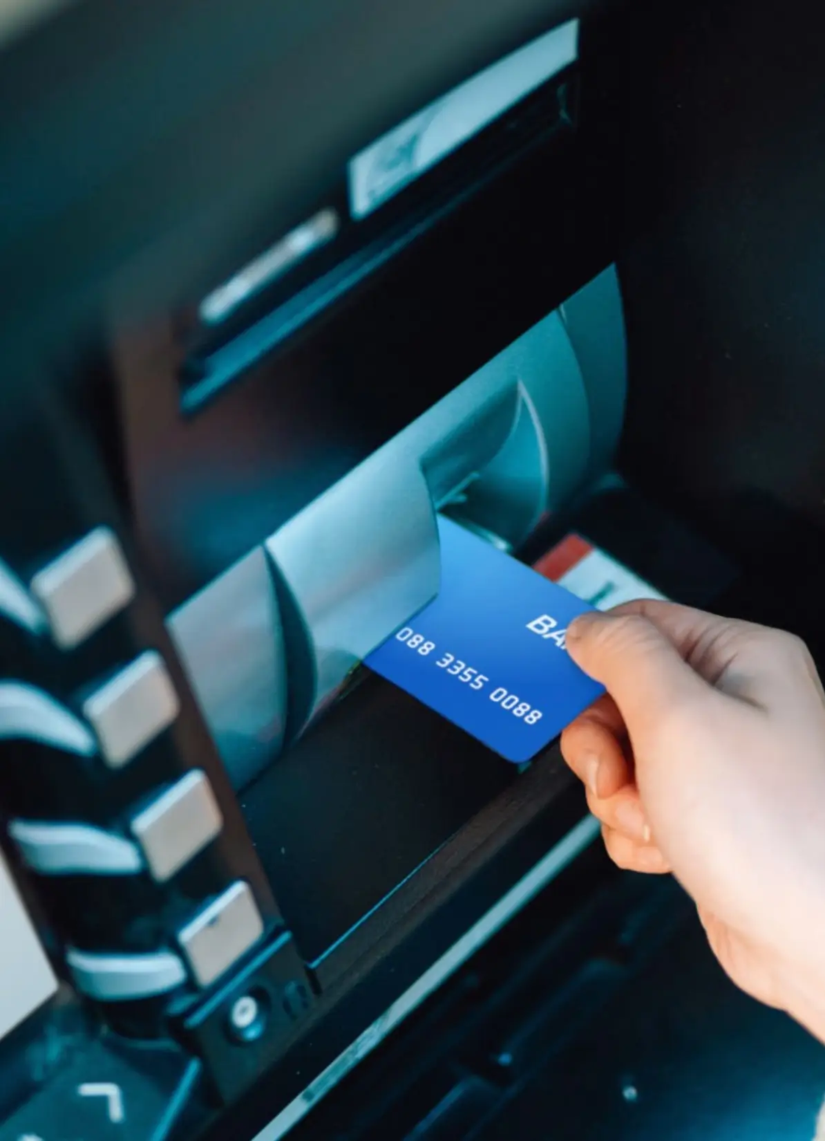 Mano inserta tarjeta bancaria azul en una máquina de cajero automático.