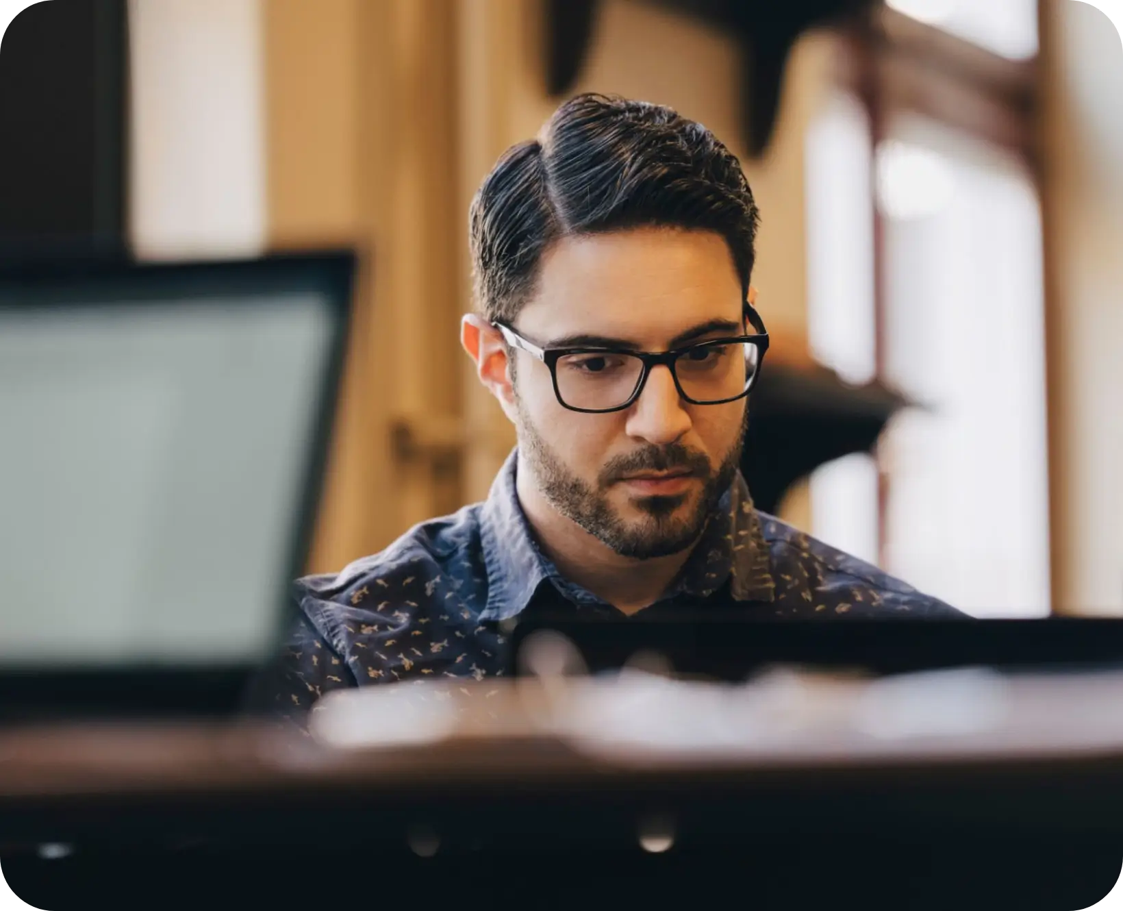 Hombre con gafas usando una computadora portátil en un espacio de trabajo interior.