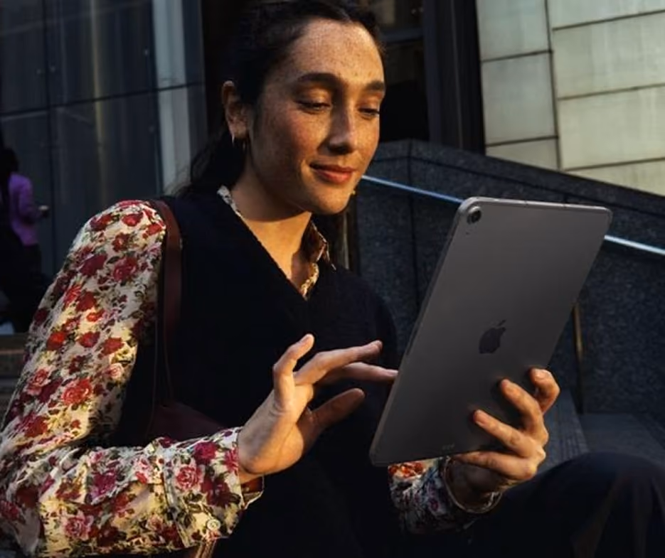 Mujer usando una tableta Apple mientras está sentada en unas escaleras al aire libre.
