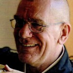 Smiling elderly man with glasses and bald head.