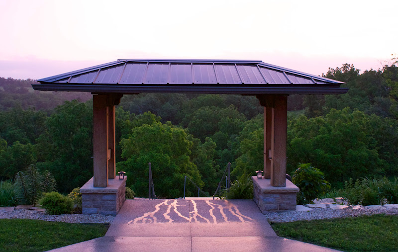 Covered outdoor entry gate with metal roof overlooking lush green trees at sunset.