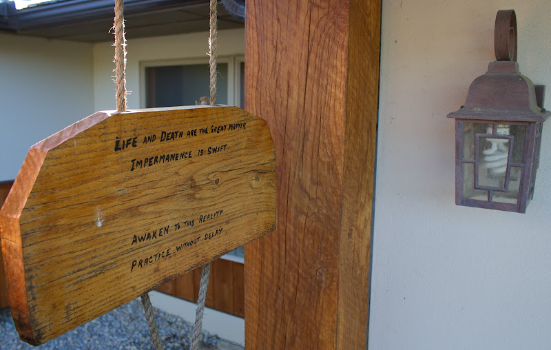 Wooden hanging sign with a rope, engraved with the text: 'Life and death are the great matter. Impermanence is swift. Awaken to this reality. Practice without delay.'