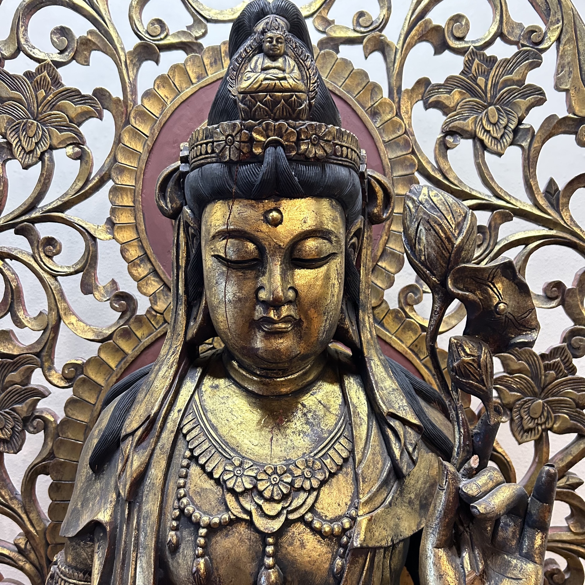 Golden statue of a serene deity with closed eyes holding a lotus flower, detailed with ornamental floral patterns and a halo.