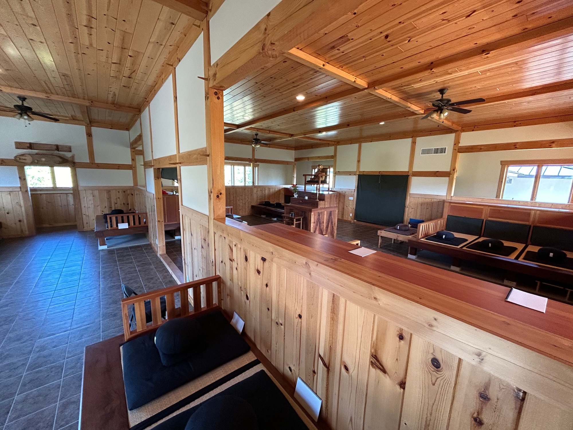 Interior of a wooden meditation hall with floor cushions and benches arranged in rows facing a central elevated platform.