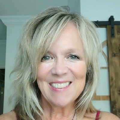 Smiling woman with shoulder-length blonde hair in a light-colored room.