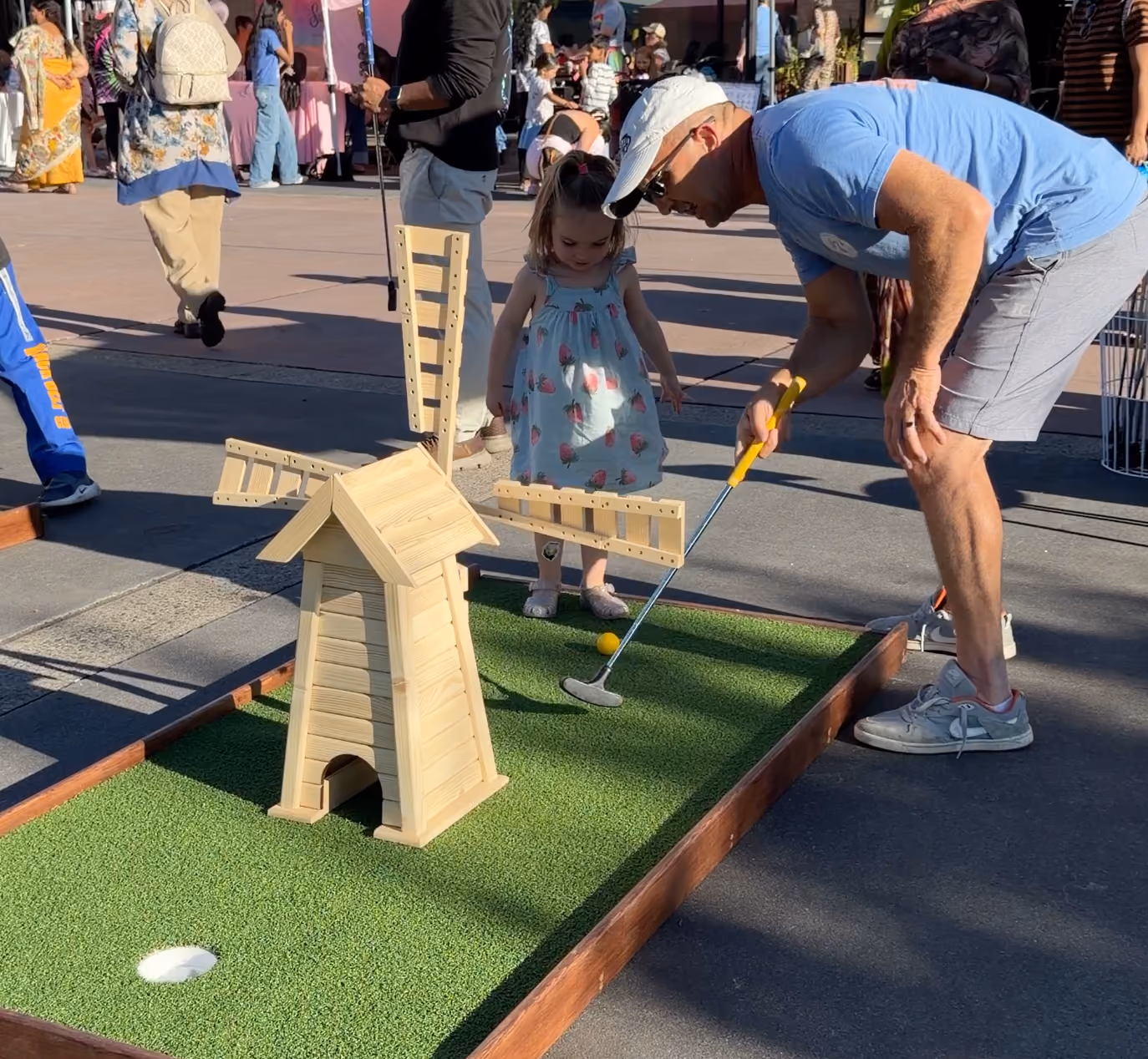 Father helping his young daughter putt through a wooden windmill obstacle