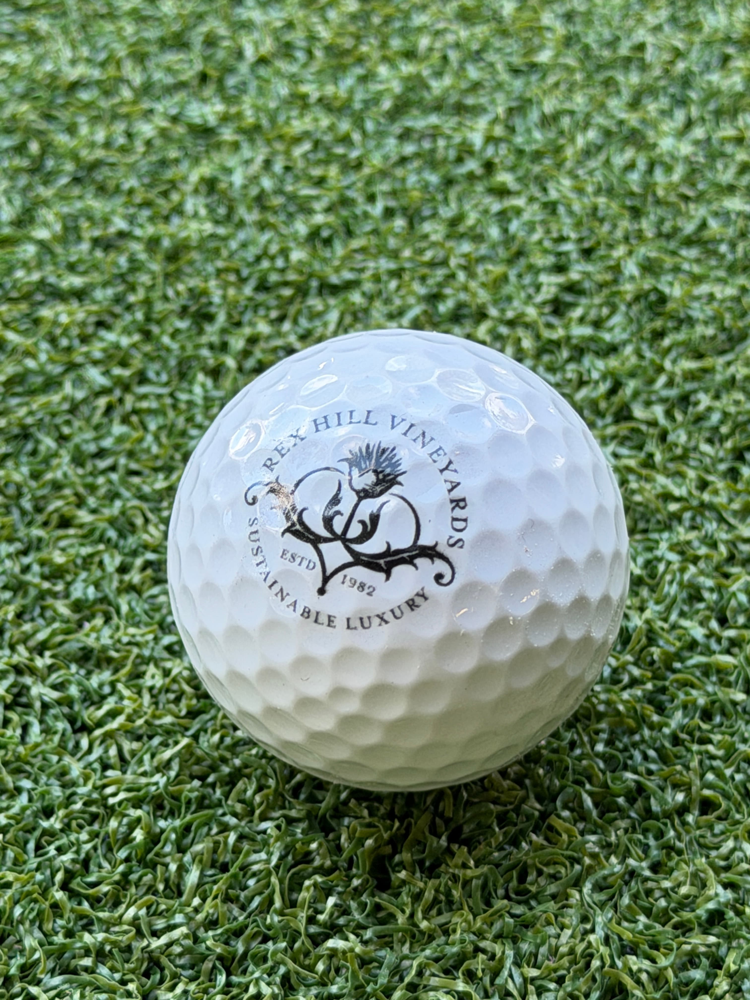 White golf ball on green artificial turf with Rex Hill Vineyards logo and text.