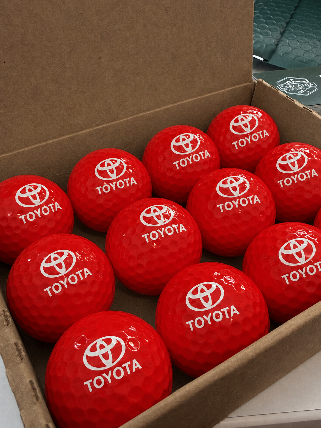 Box of bright red Toyota-branded golf balls arranged in neat rows inside a cardboard box.