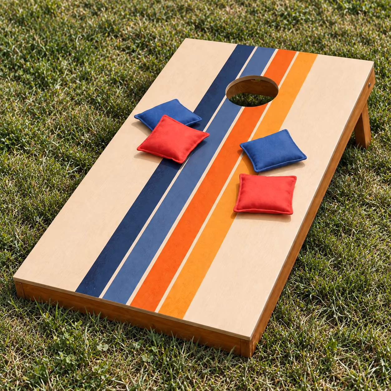 Wooden cornhole board with blue and orange stripes and red and blue beanbags on a lawn.