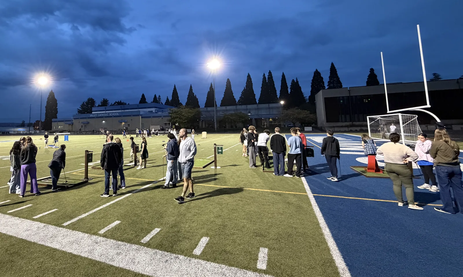 Mini golf players on Valley Catholic's field under stadium lights at dusk