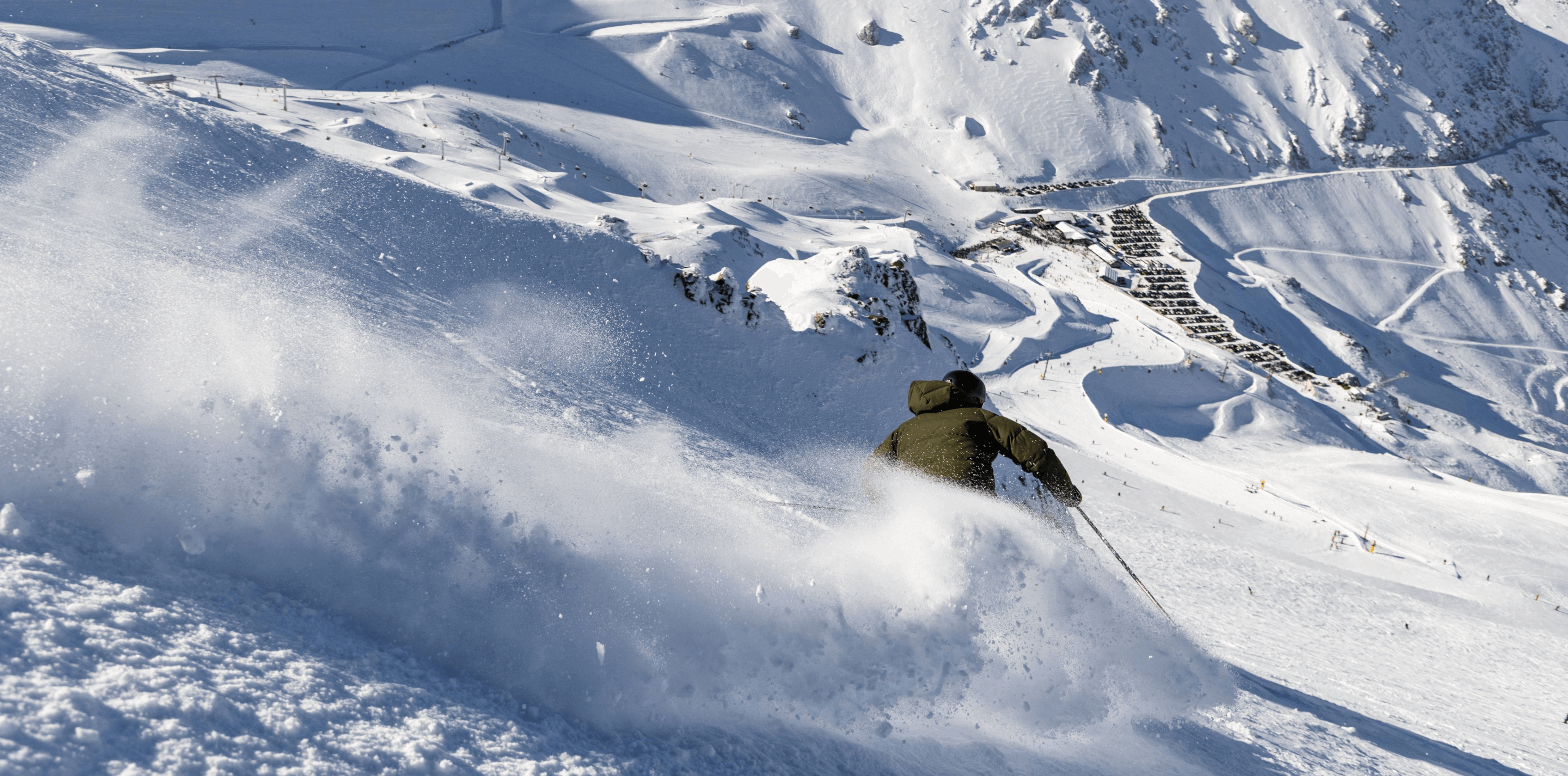 Skier carving through fresh powder above wide alpine terrain at Mt Hutt on a clear day