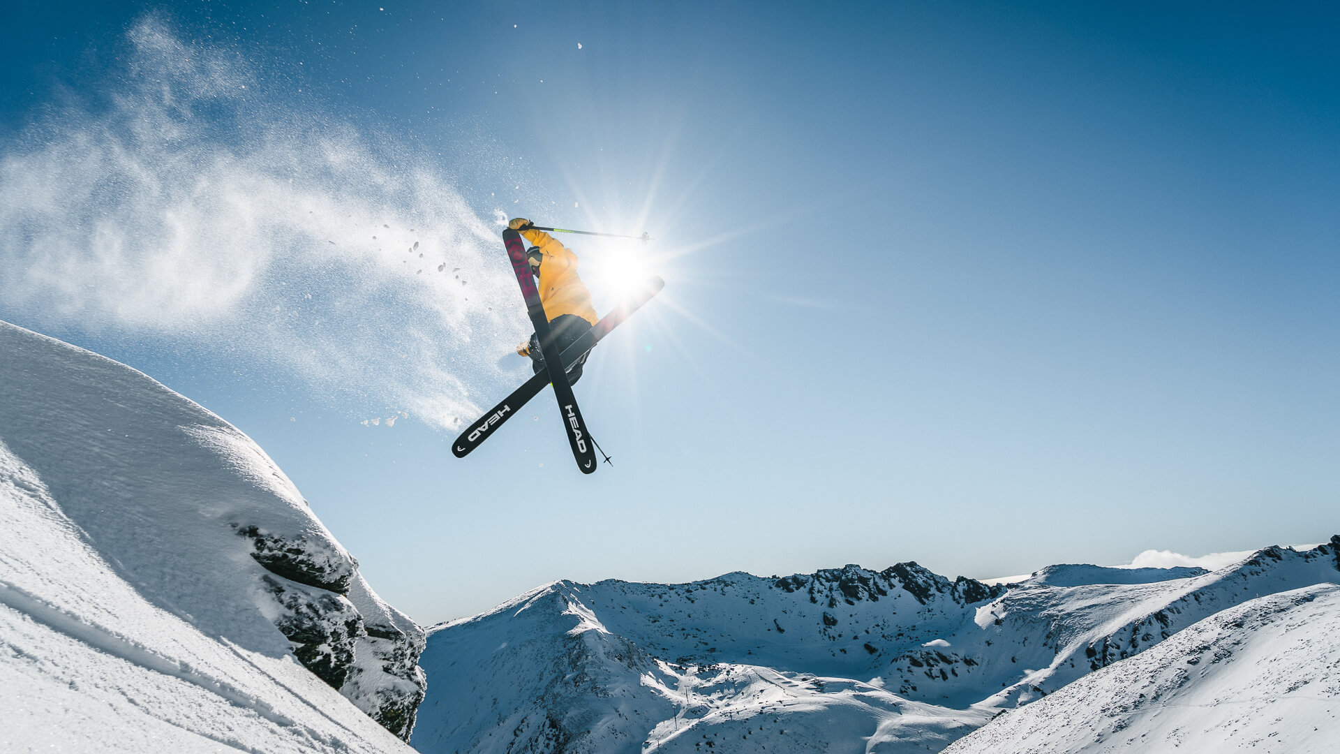 Skier performing a jump with snow spray in alpine terrain at Mt Hutt on a clear day