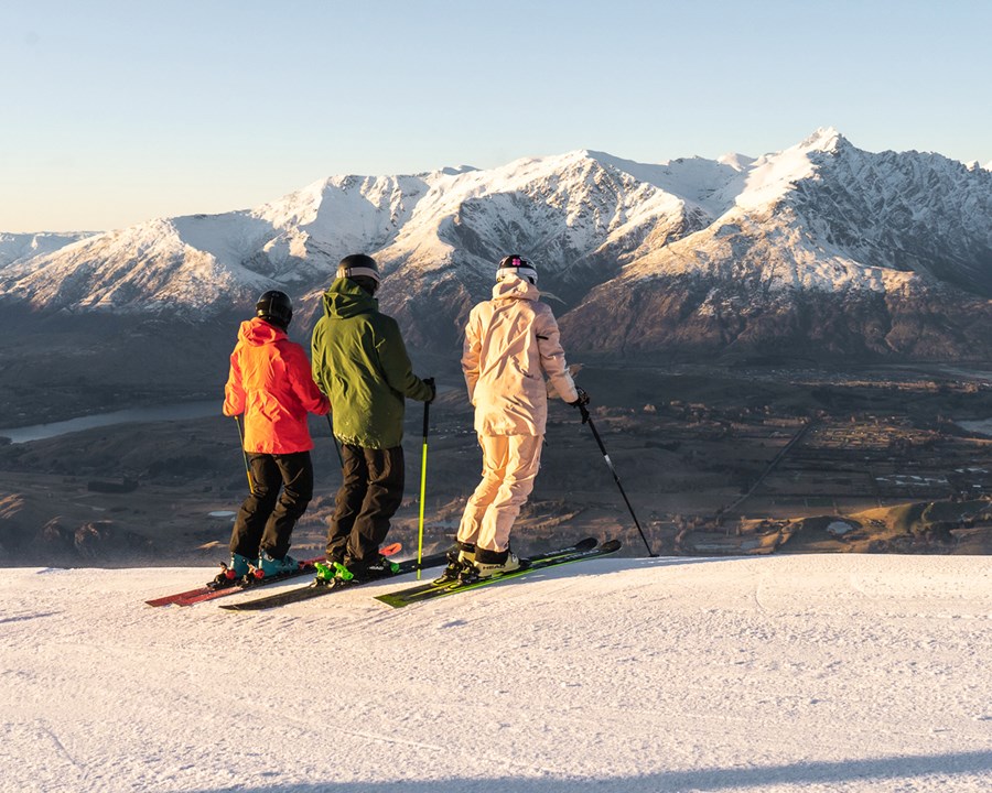 Skiers standing at edge of mountain facing snow covered mountain.