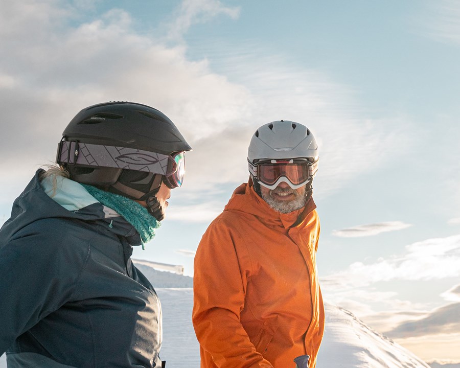 Two skiiers smiling, wearing helmets.