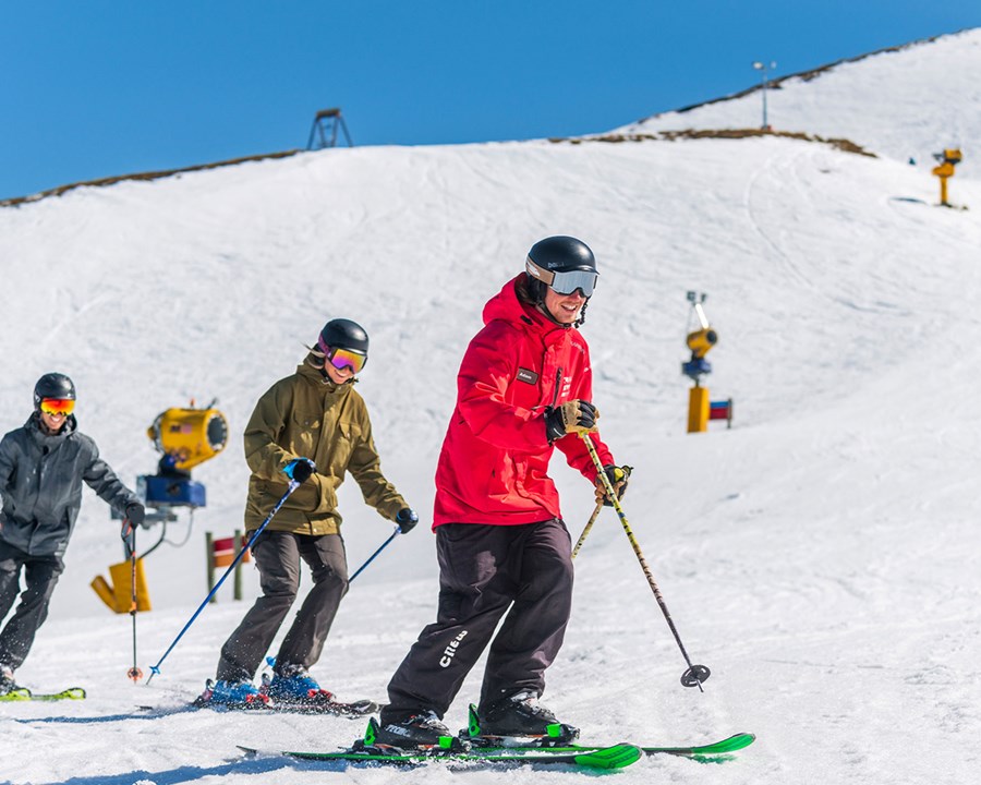 Ski instructor skiing down slope with two smiling skiers trailing behind.