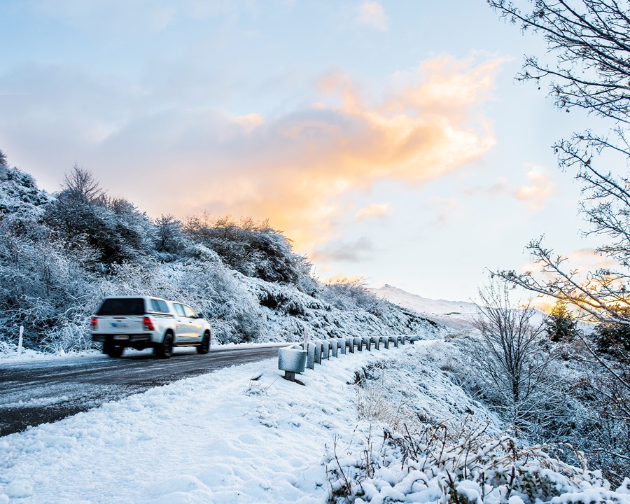 White ute driving on snow-covered alpine road.