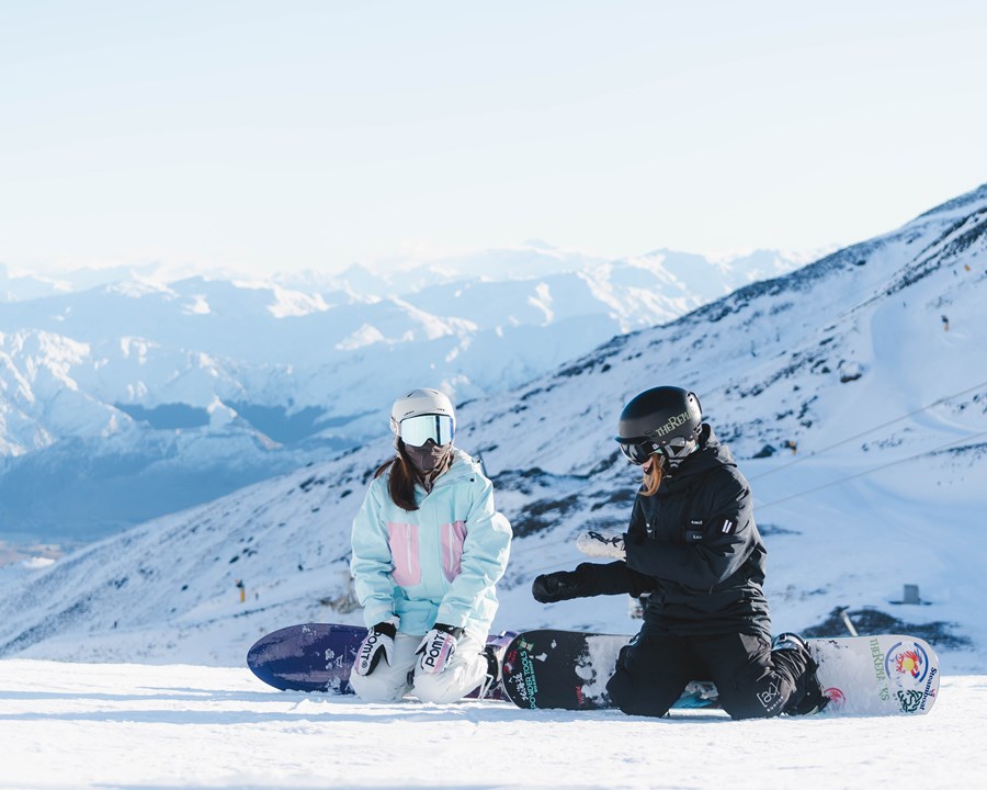 Snowboarding instructor kneeling on slope talking to snowboarder