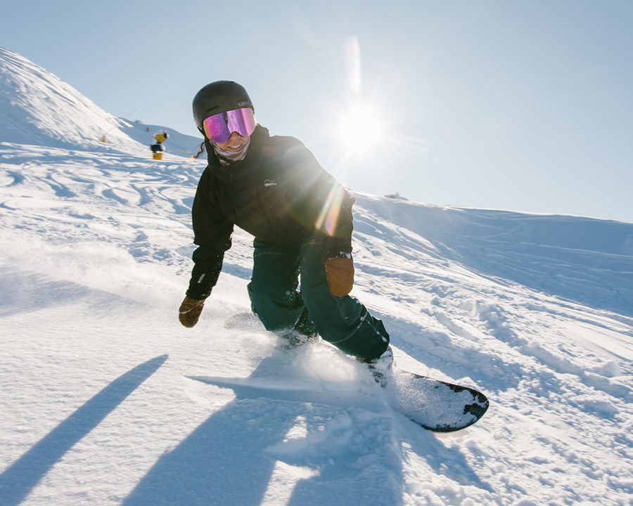 Woman smiling while snowboarding down slope.