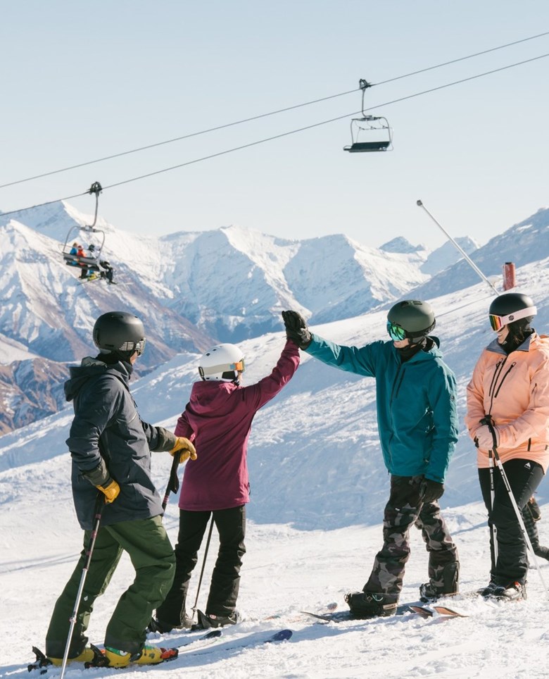 Group high fiving on slope on bright sunny day.