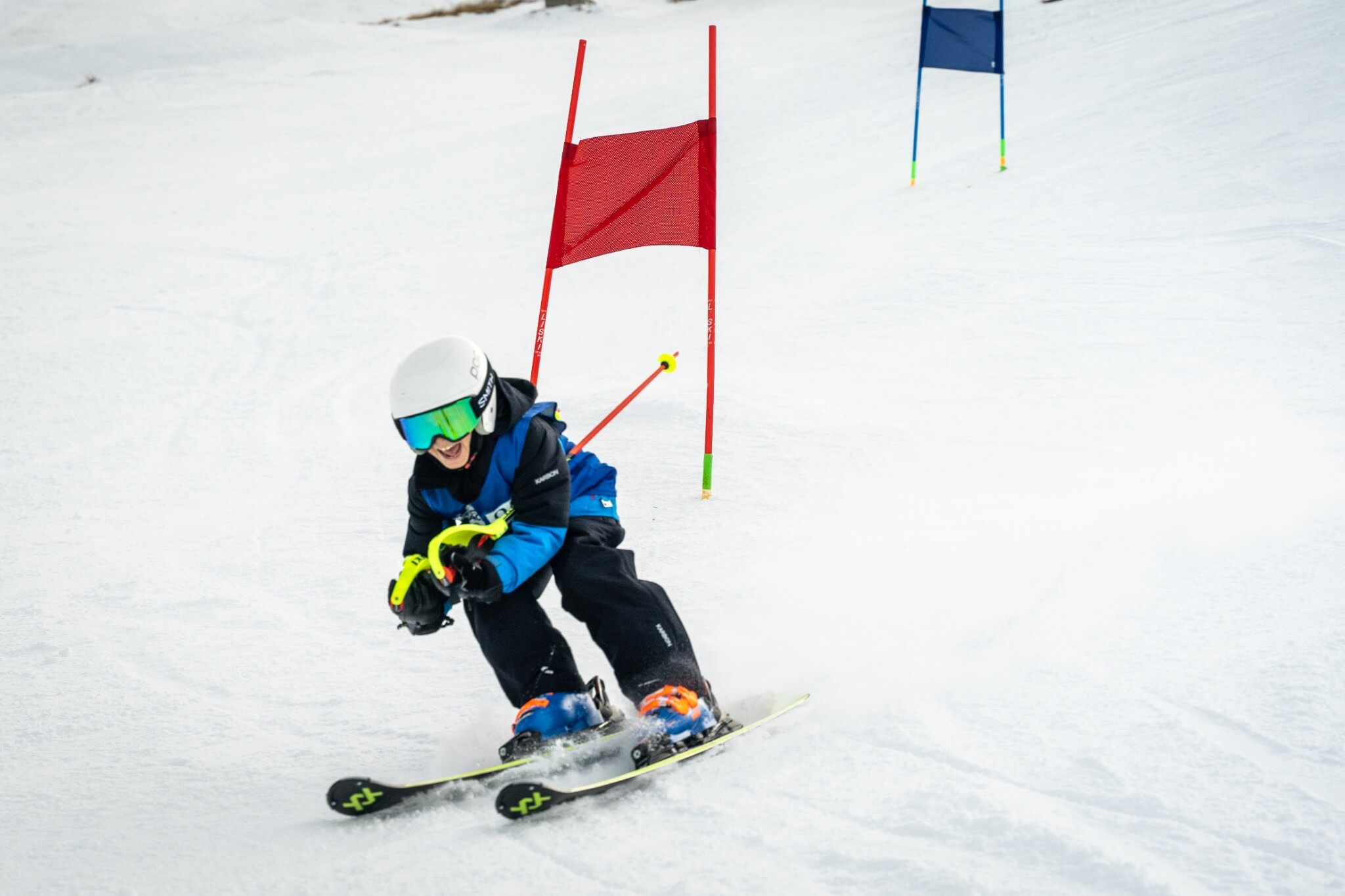 Young skier wearing a helmet and goggles skiing aggressively past red slalom gates in snow.