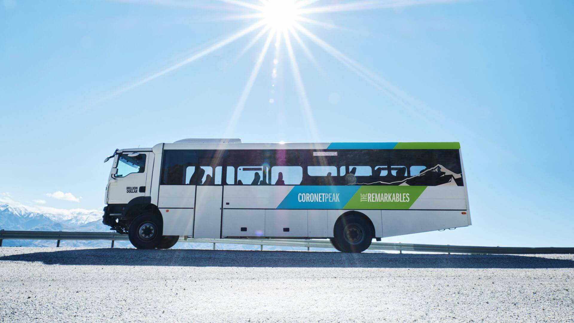 Side view of a white Coronet Peak The Remarkables ski bus under a bright sun with mountains in the background.