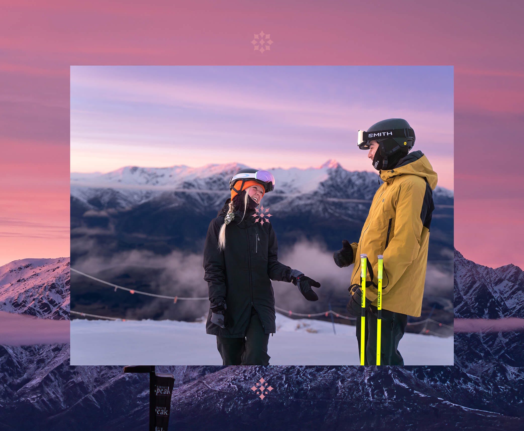 Two skiers in winter gear chatting with snowy mountains and purple sky at sunset behind them.