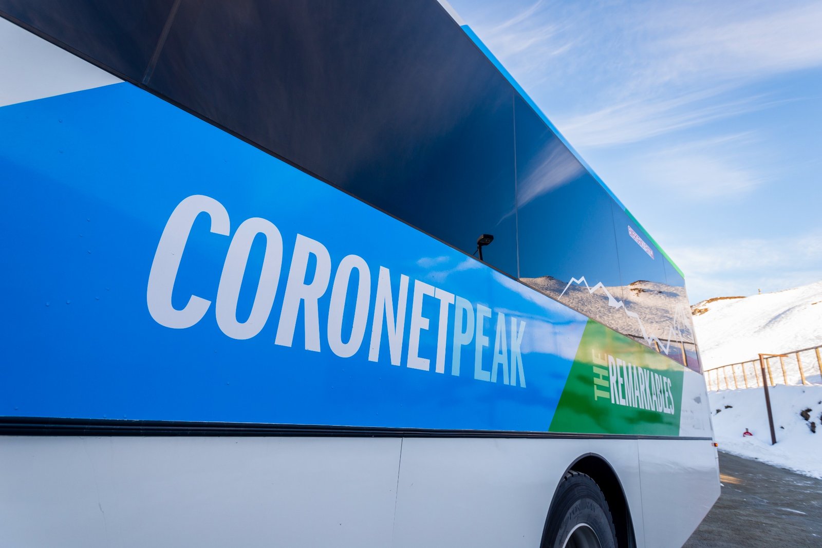 Blue and green bus with the text CORONET PEAK and THE REMARKABLES parked near snowy mountains.