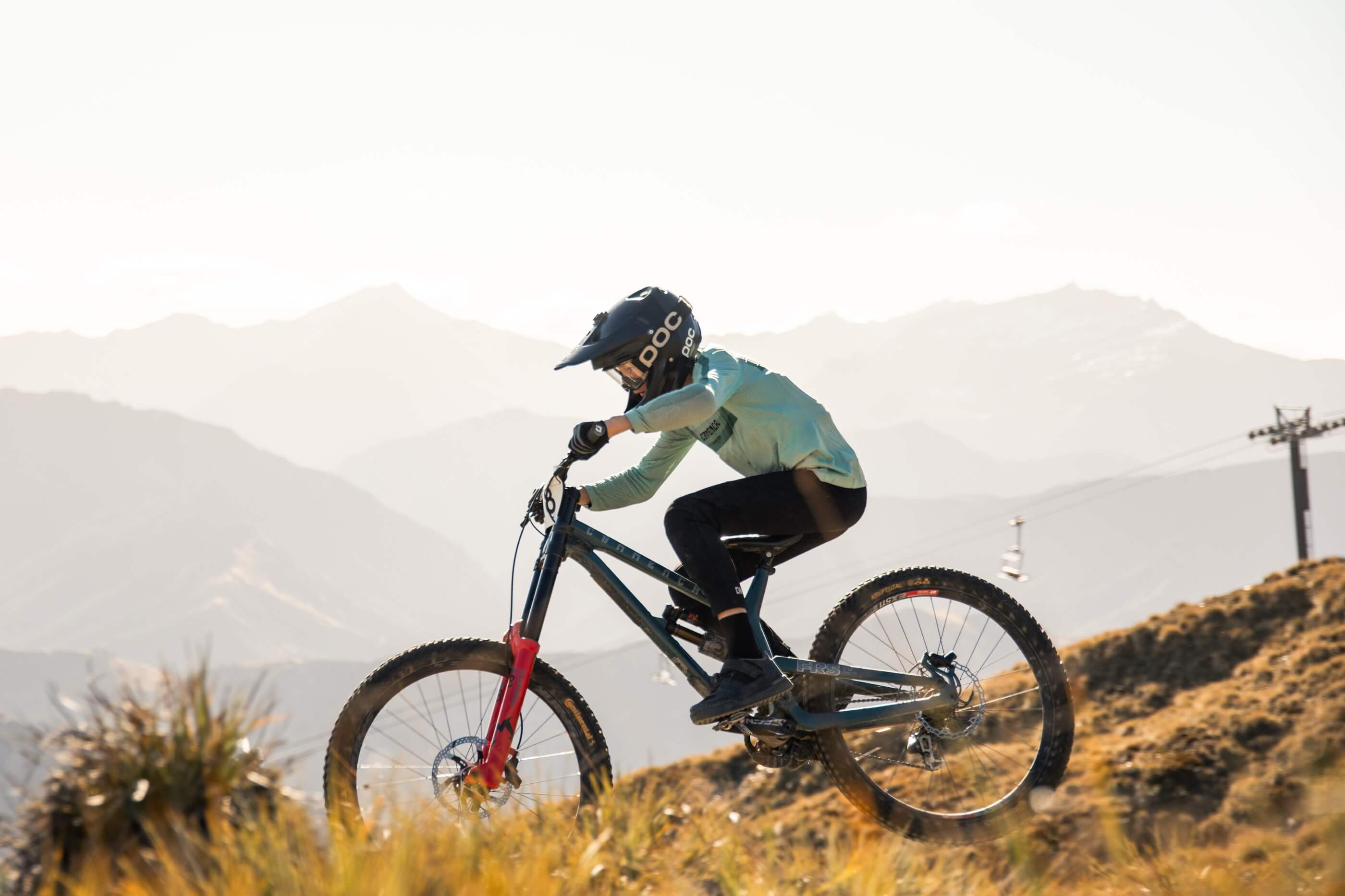 Person wearing helmet riding a mountain bike on a trail with mountains in the background.