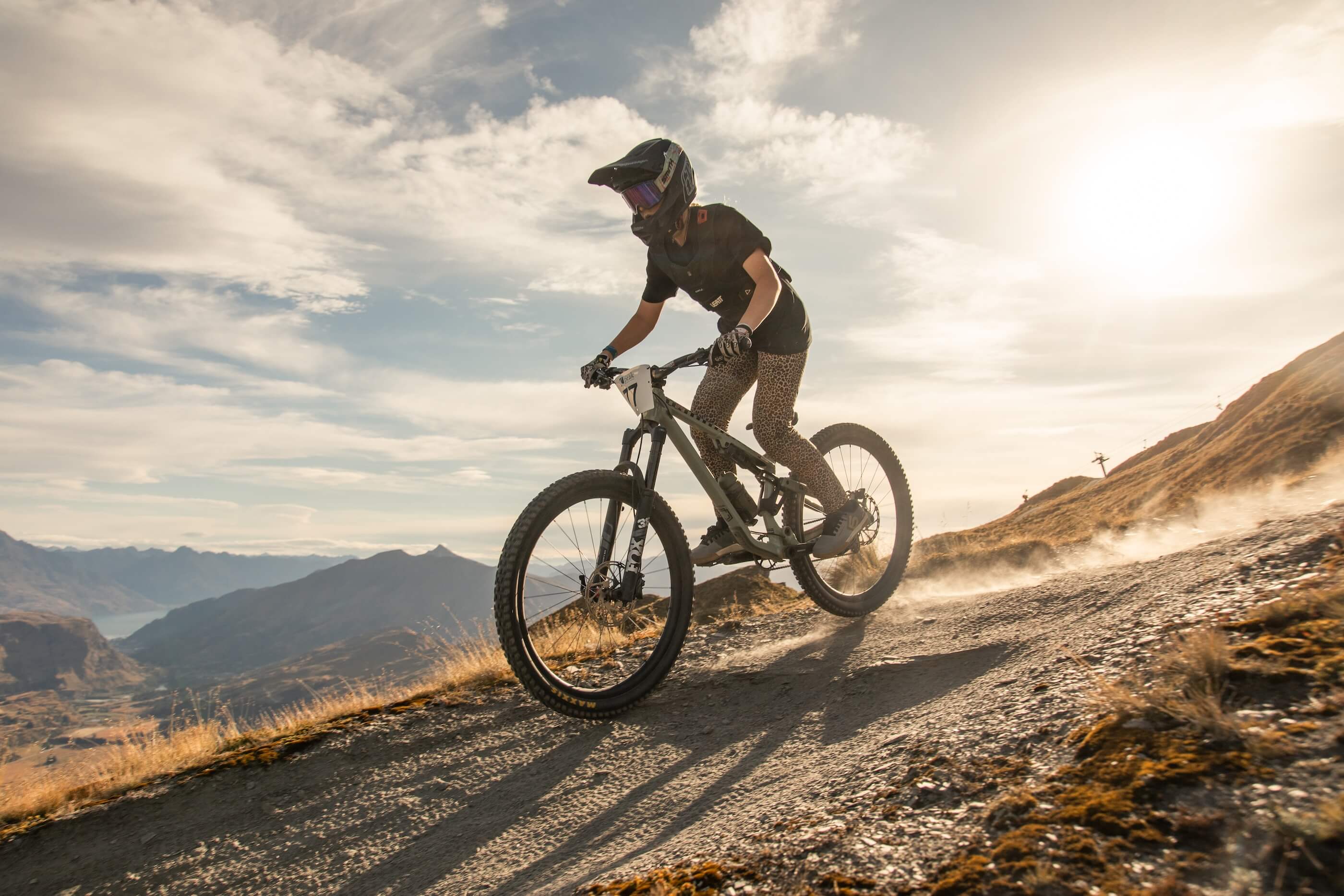 Person wearing helmet rides a mountain bike downhill on a rocky trail at sunset.