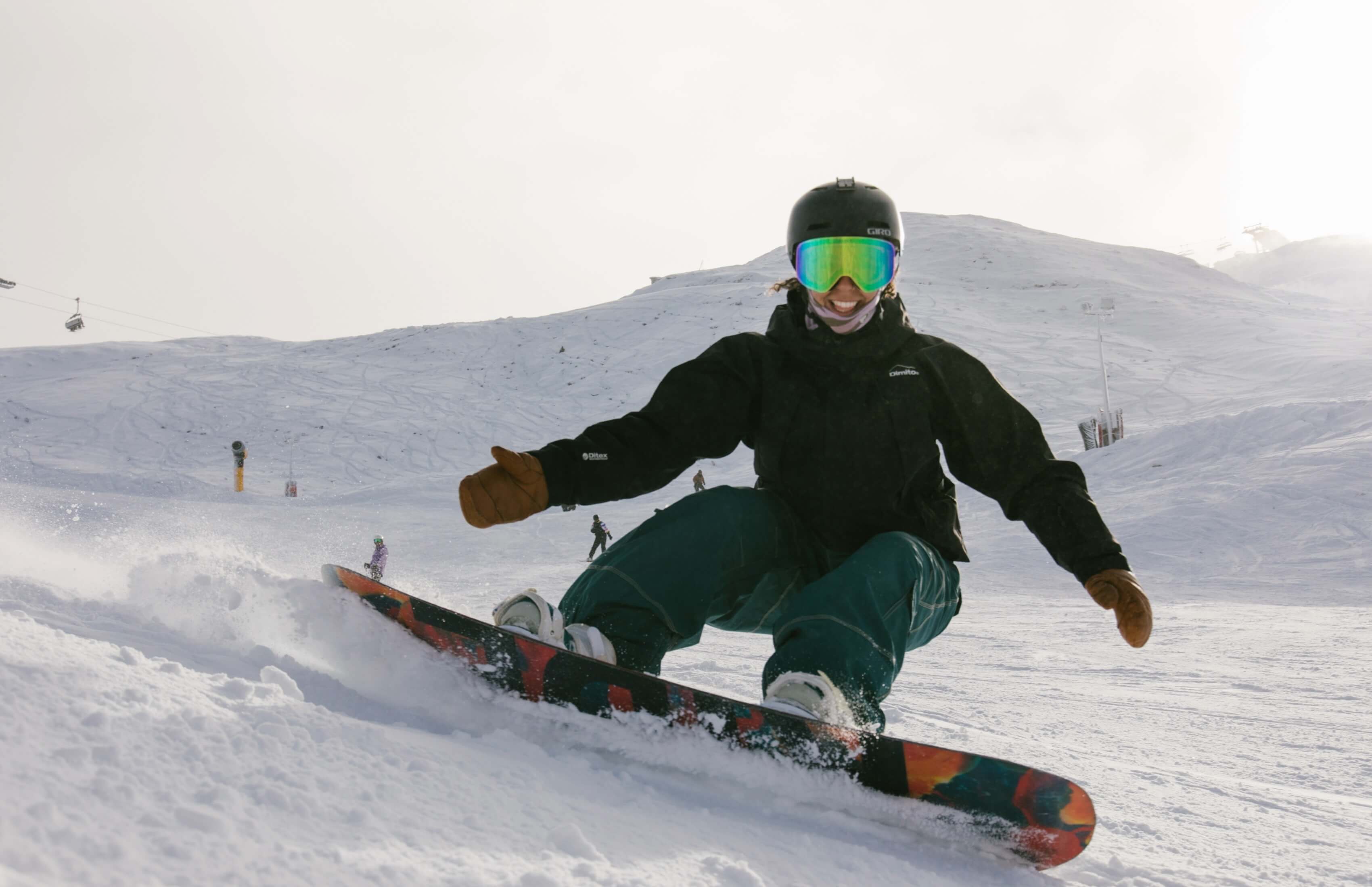 Person snowboarding down a snowy slope wearing a black jacket, helmet, and reflective goggles.