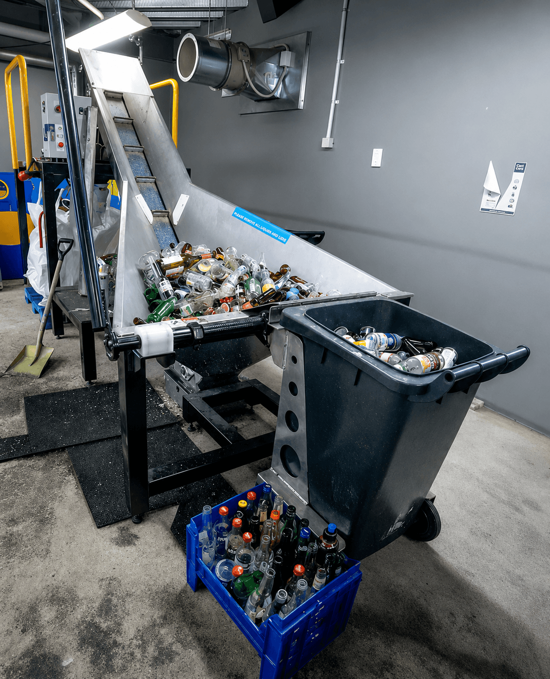 Recycling station with glass bottles in a bin, crate, and on a conveyor belt indoors.