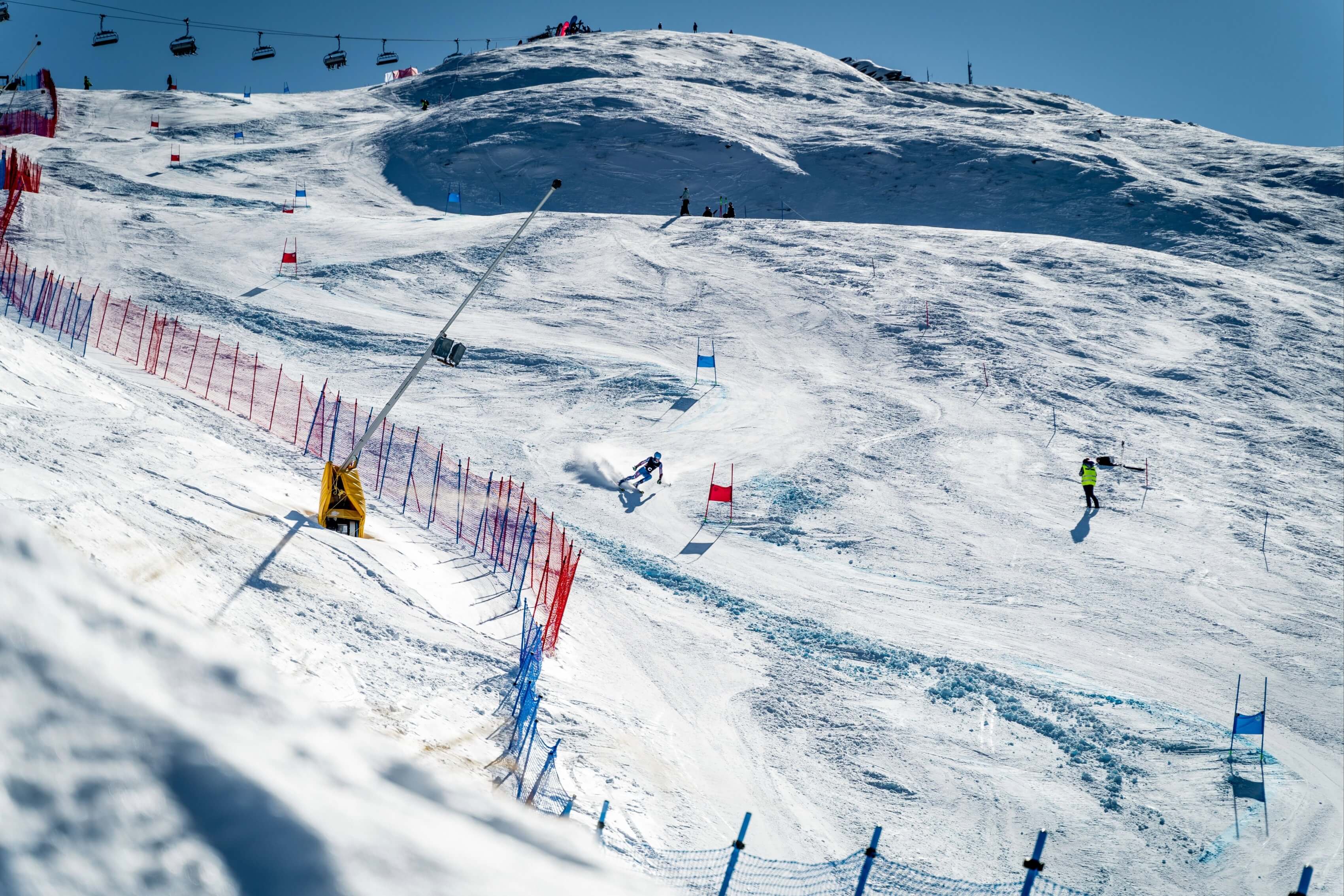 Skier racing down a snowy slalom course marked with red and blue gates on a sunny day.