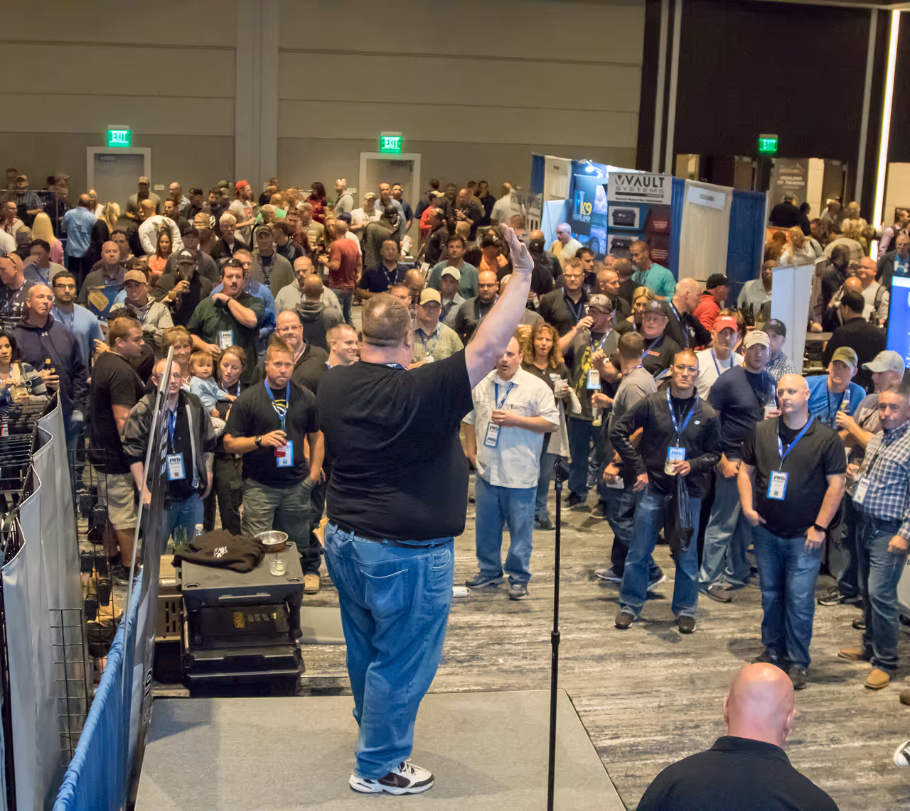 Man on stage raising hand while addressing a large crowd at an indoor event or conference.