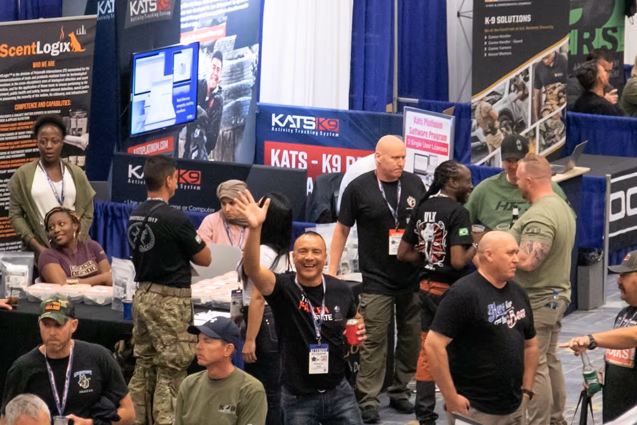 People at a conference booth with banners, one man smiling and waving at the camera.
