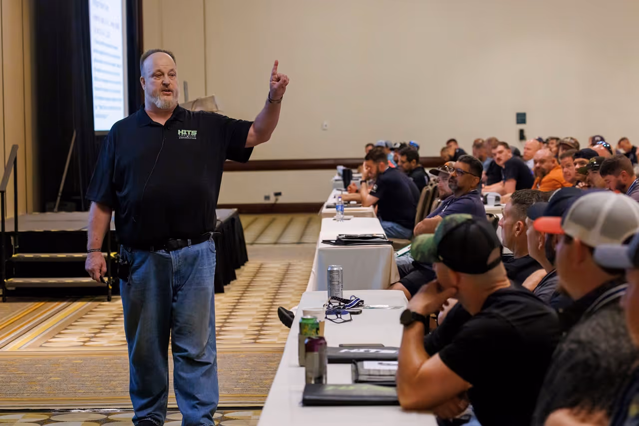 Man in black shirt teaching a room of seated adults in a conference setting.