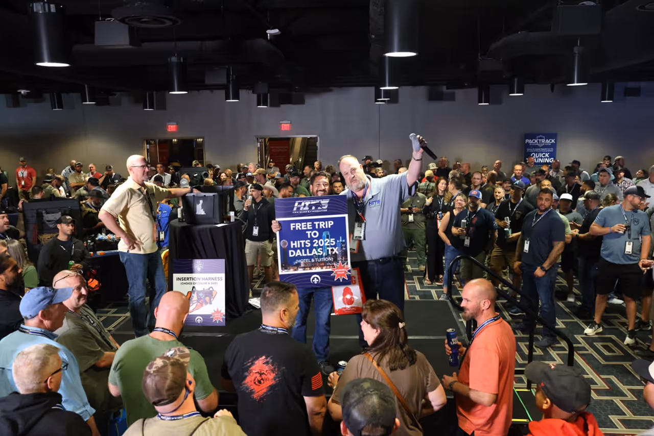 Man holding sign for free trip to HITS 2025 Dallas at event with large crowd and announcer.