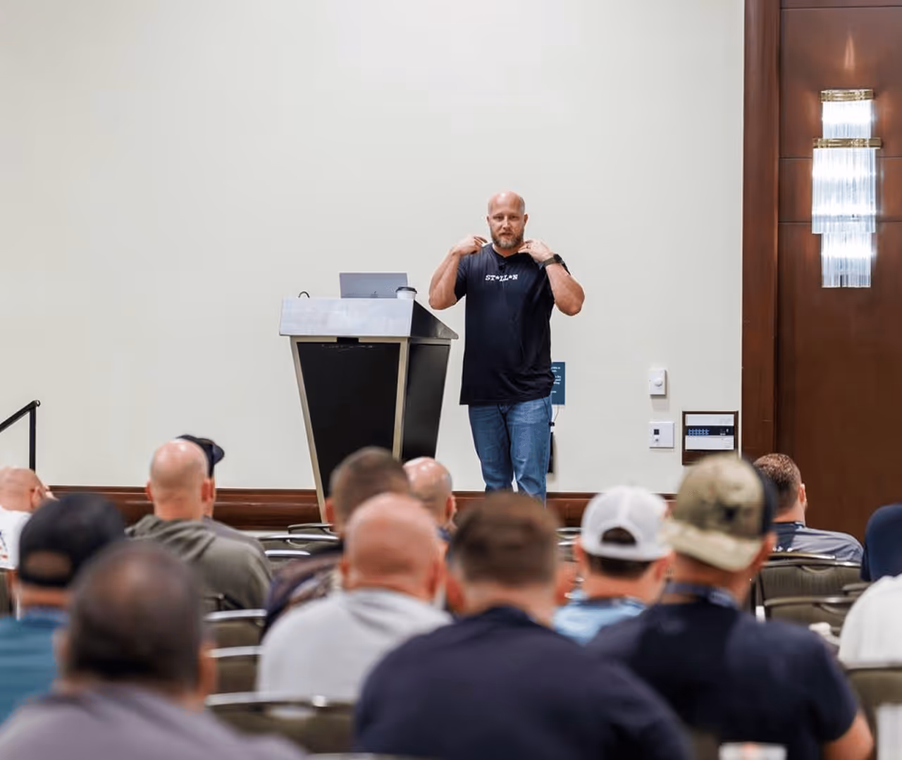 Conference speaker addressing a packed room of K-9 handlers and trainers from the podium at HITS