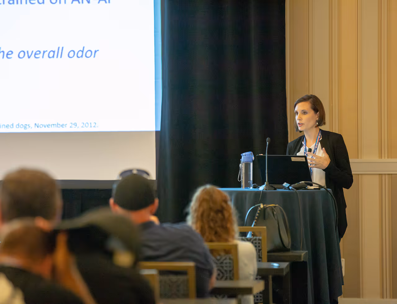 Woman giving a presentation with a laptop and microphone to an audience in a conference room.