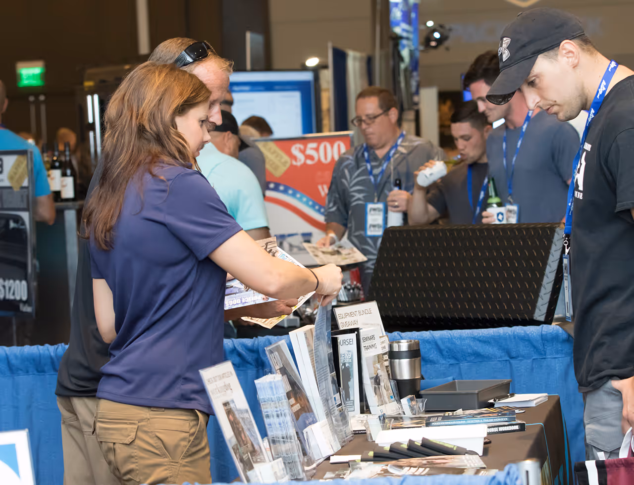 People looking at brochures and materials on a trade show or vendor booth table.