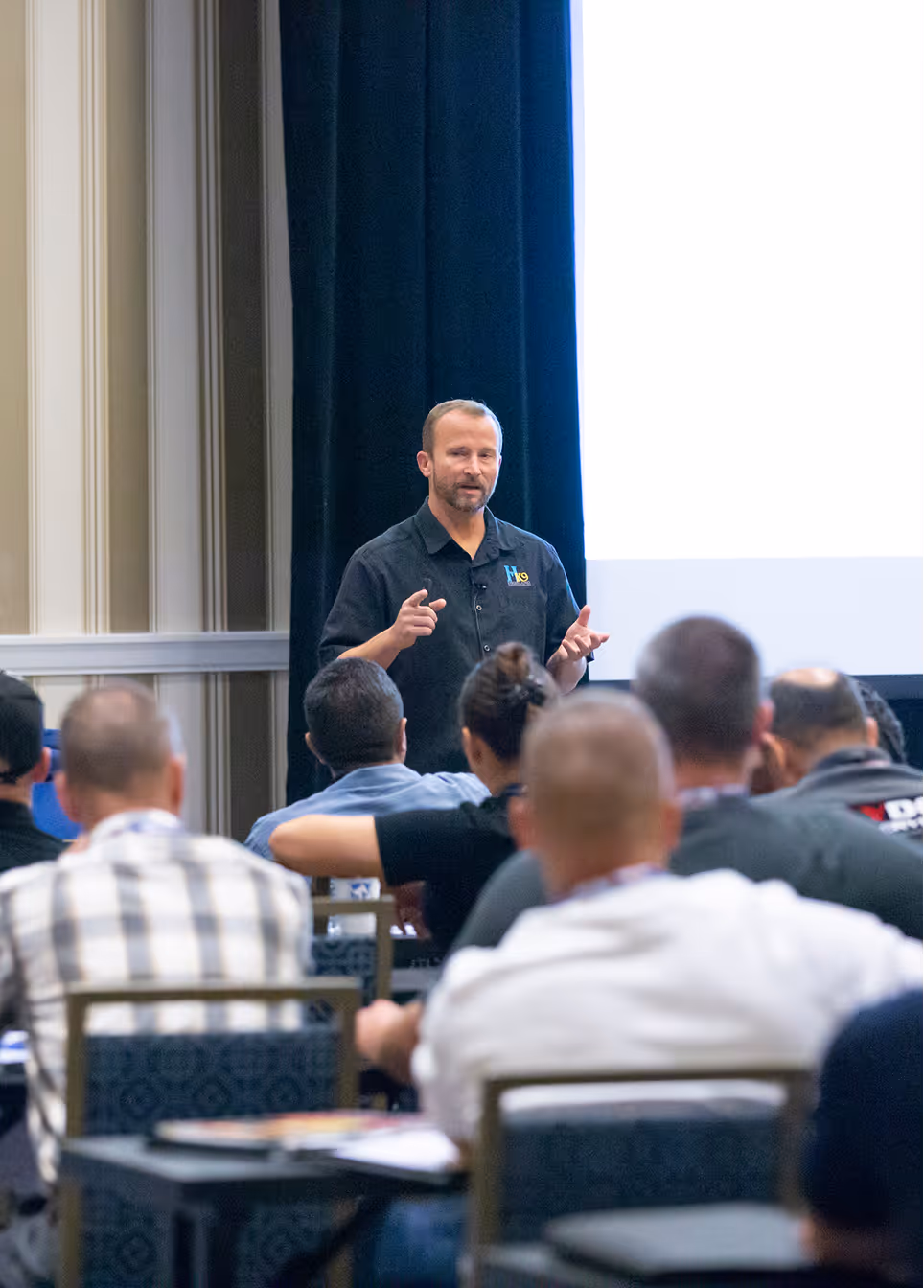 Man in black shirt giving a presentation to seated audience in a conference room.
