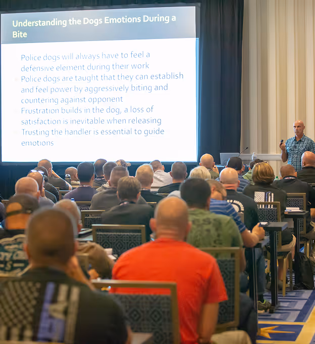 Audience attending a lecture on police dogs' emotions during a bite with speaker and presentation slide.
