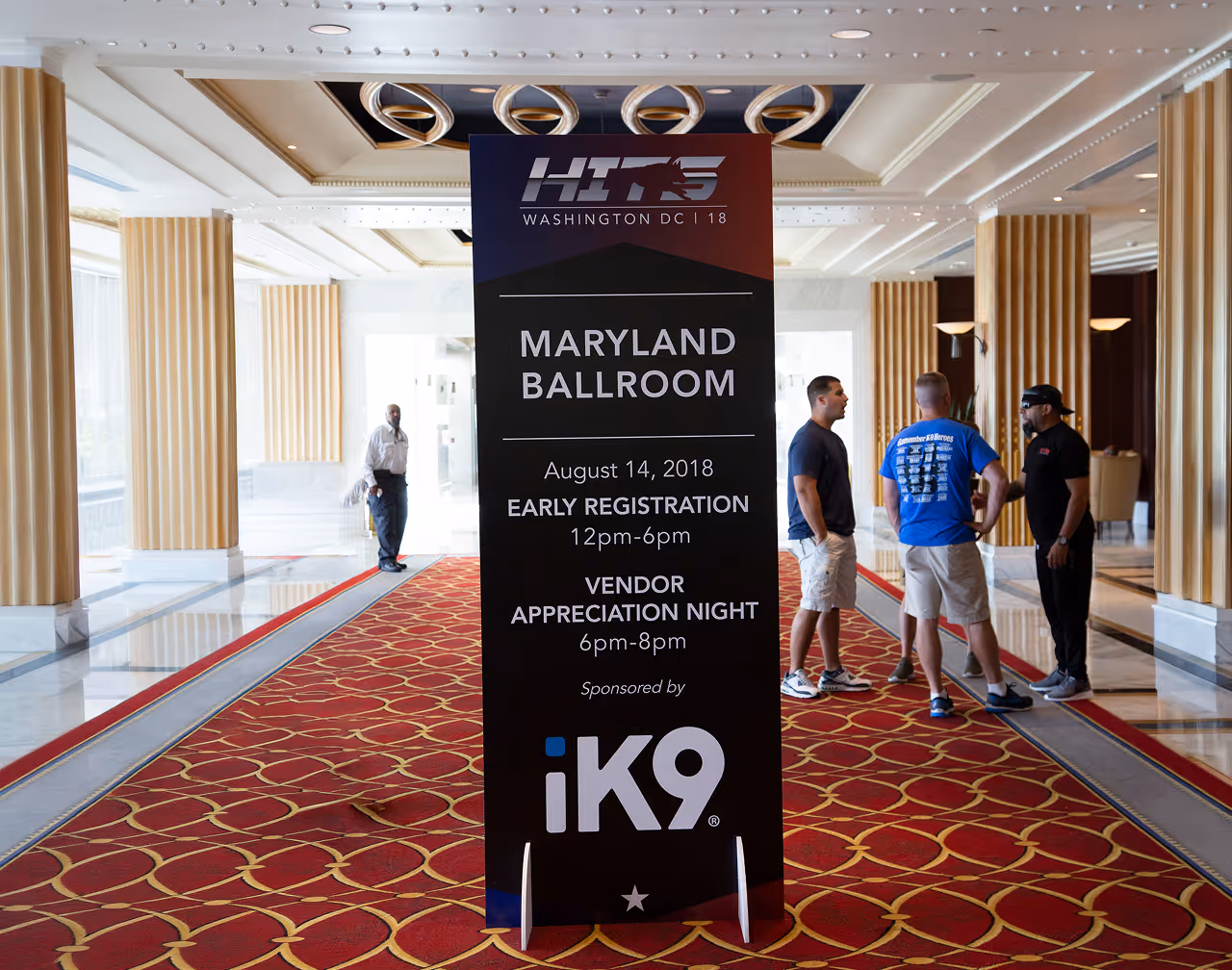 Sign for Maryland Ballroom event with registration and vendor night details, three men talking nearby.