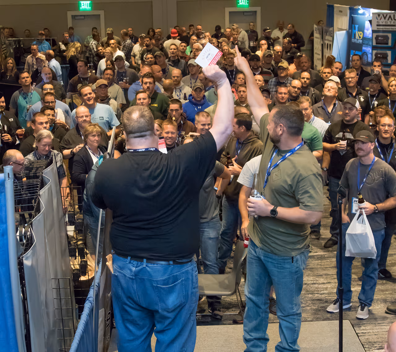 Crowd watching two men on stage holding up raffle tickets at an event or conference.
