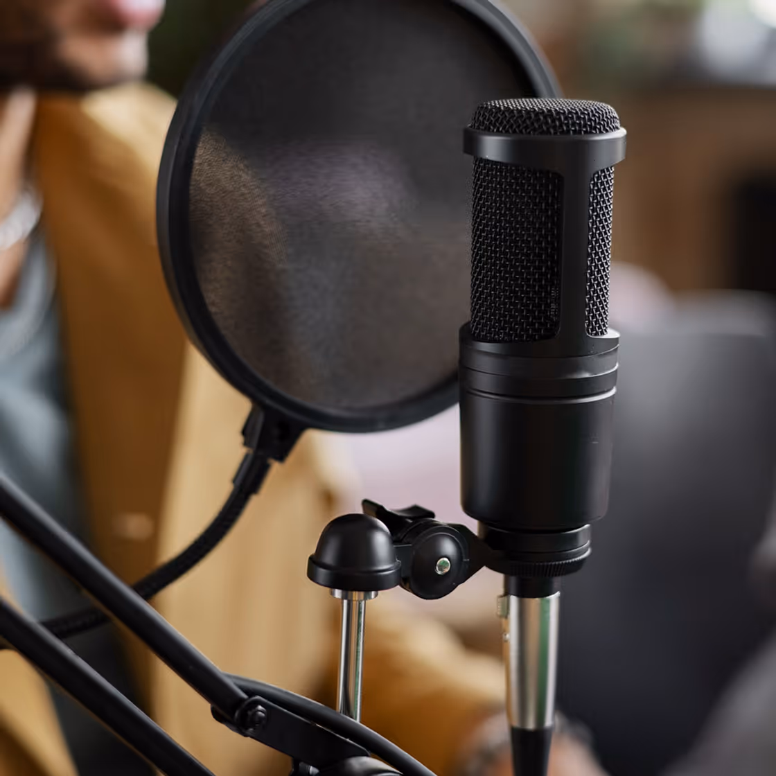 Close-up of a black studio microphone with a pop filter and part of a person in the background.