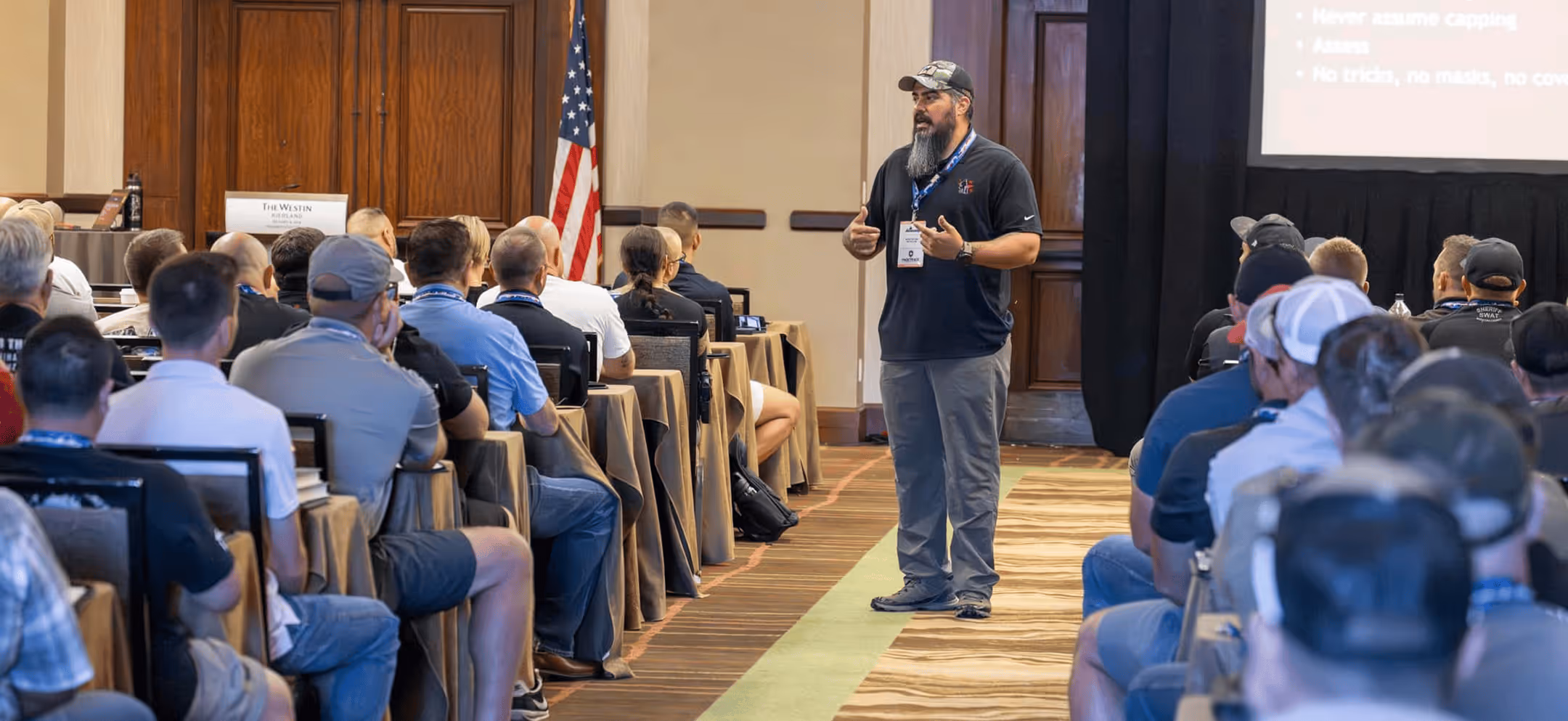 K-9 training instructor presenting tactical assessment principles to a packed ballroom of law-enforcement handlers at a HITS conference seminar