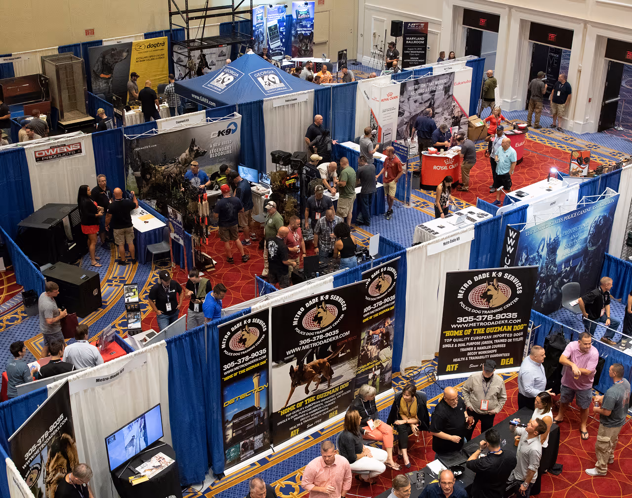 Overhead view of people visiting booths at a police K-9 services and dog training expo indoors.