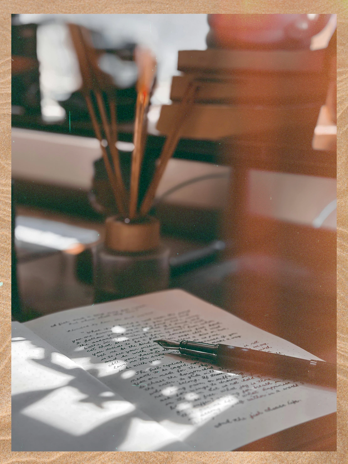 Open journal with handwritten text and a fountain pen resting on the page, with a blurred background of paintbrushes in a jar.