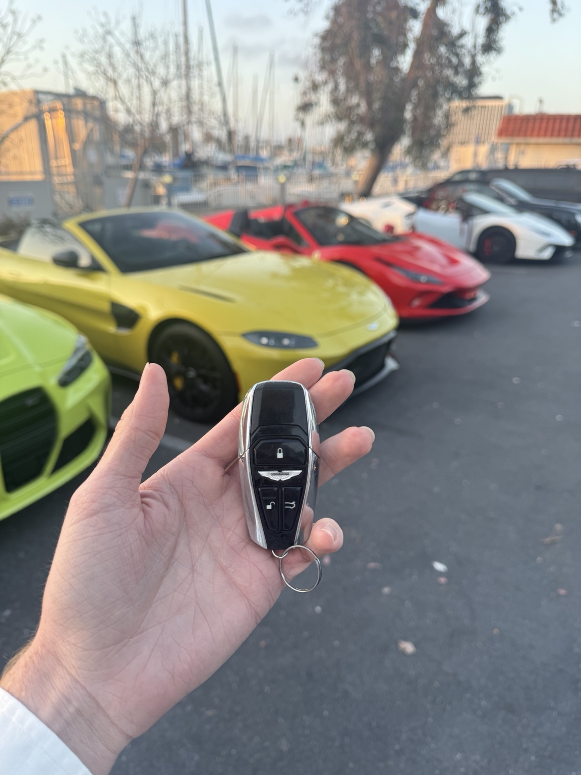 An Aston Martin key in front of a line of exotic cars at a Southern California marina