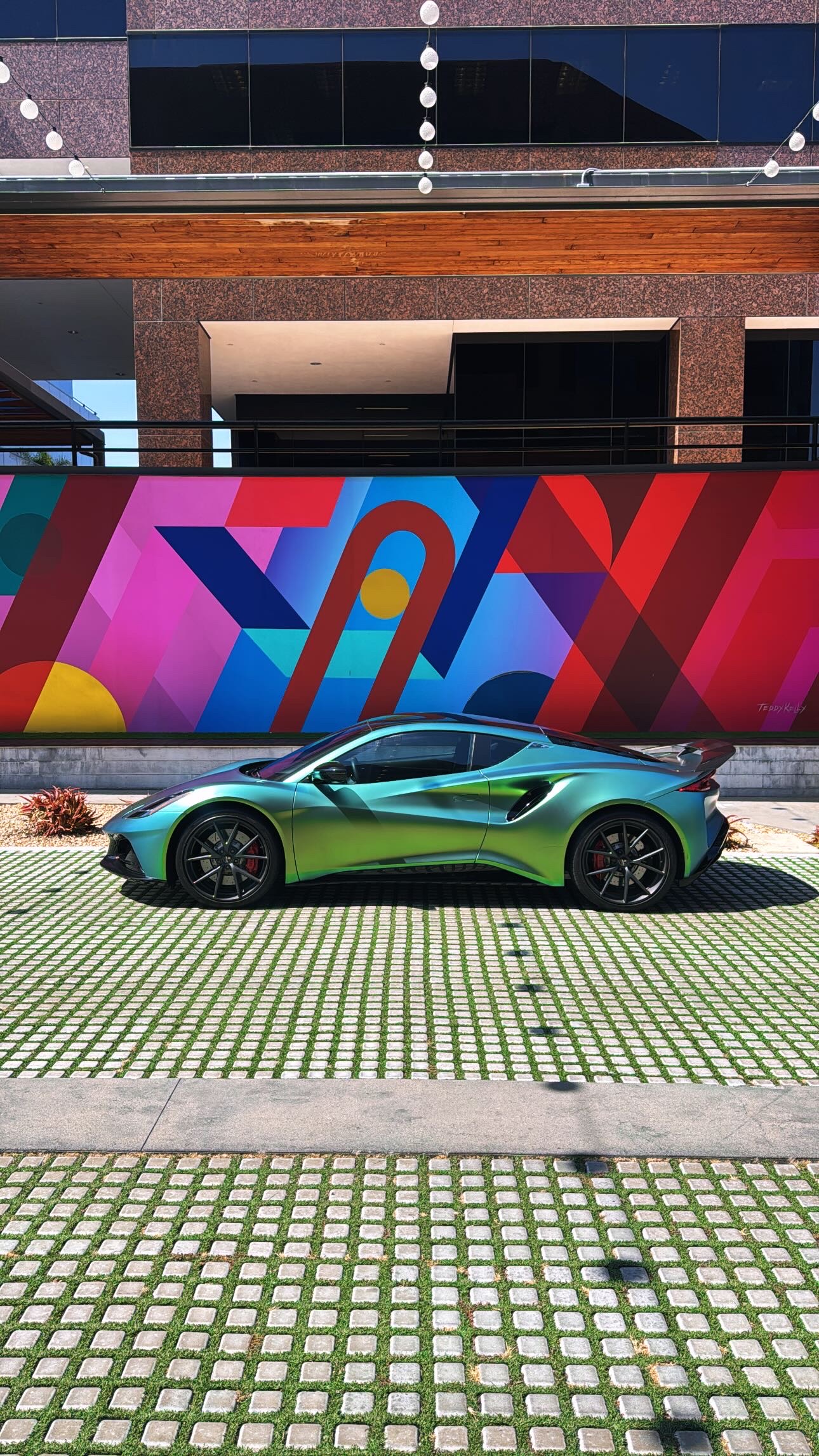 A colour-shifting green Lotus Emira parked in front of a geometric mural in Southern California