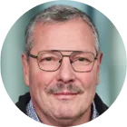 Porträt eines älteren Mannes mit Brille, grauen Haaren und Schnurrbart.